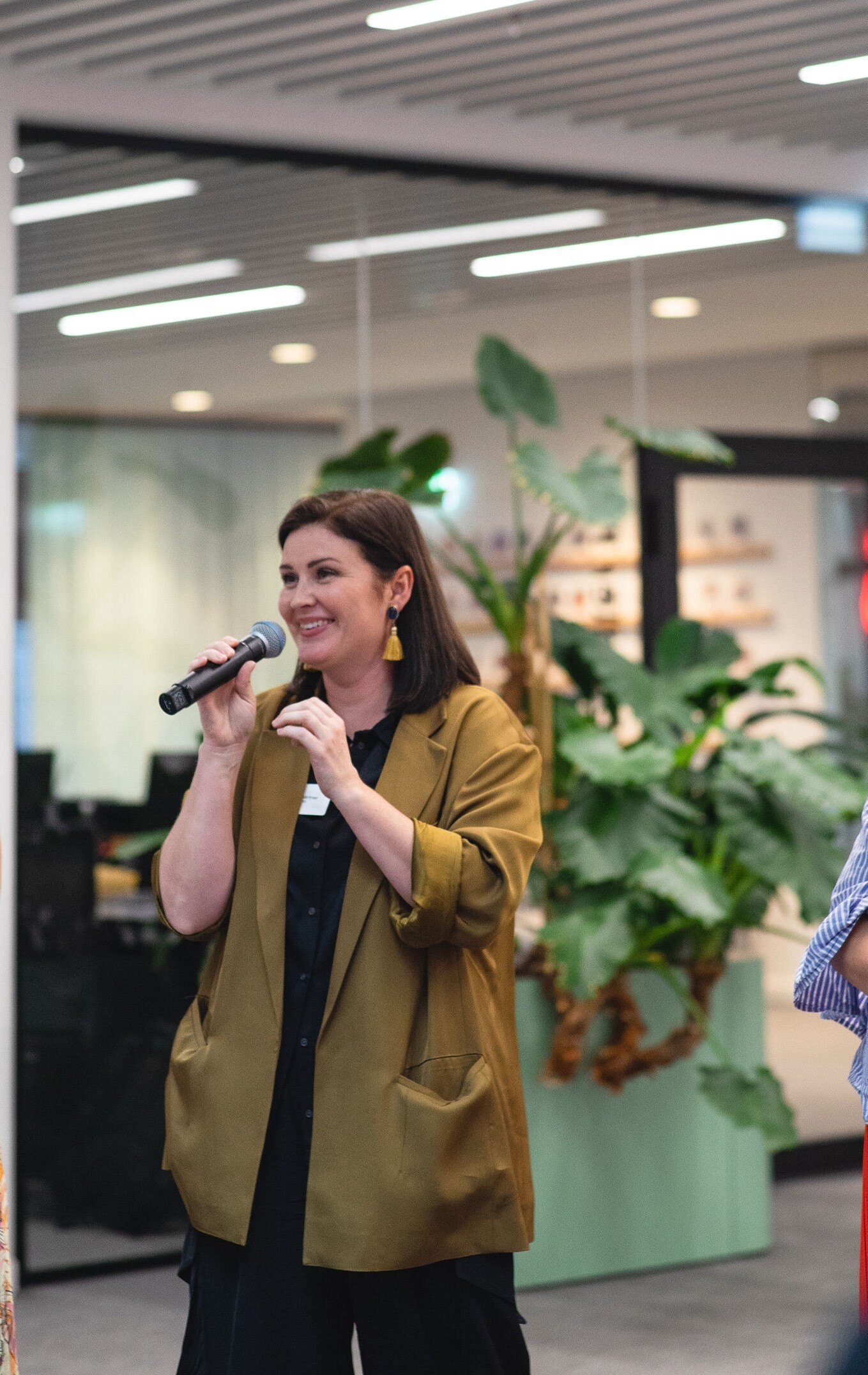 Close-up of a woman speaking into a microphone, with plants visible in the background.