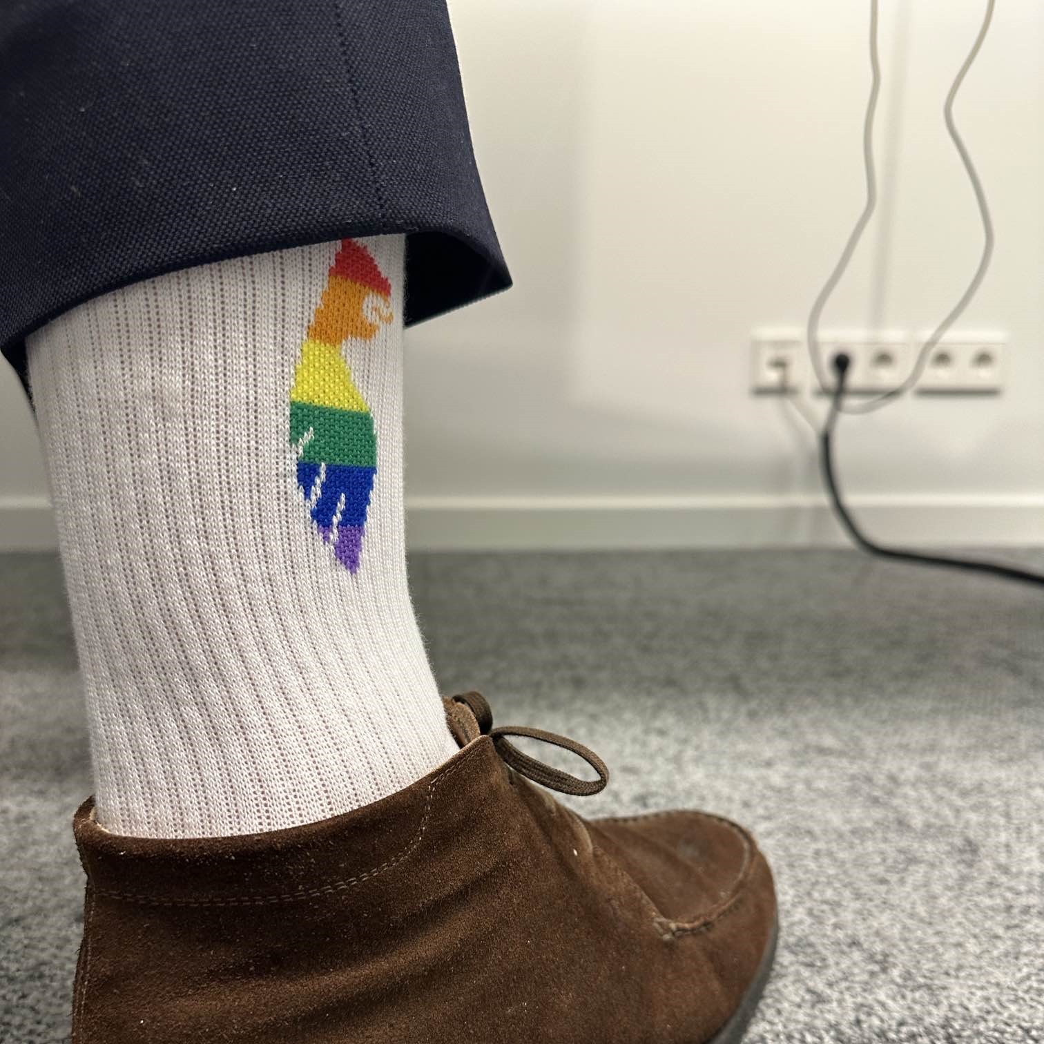 Ein Bein mit einer weißen Socke, auf der ein Regenbogenlogo abgebildet ist.