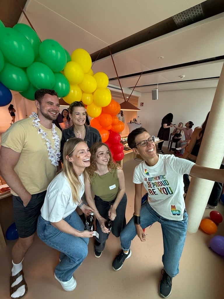 Eine Gruppe von fünf Personen posiert für ein Foto in einem Raum, der mit bunten Luftballons dekoriert ist.