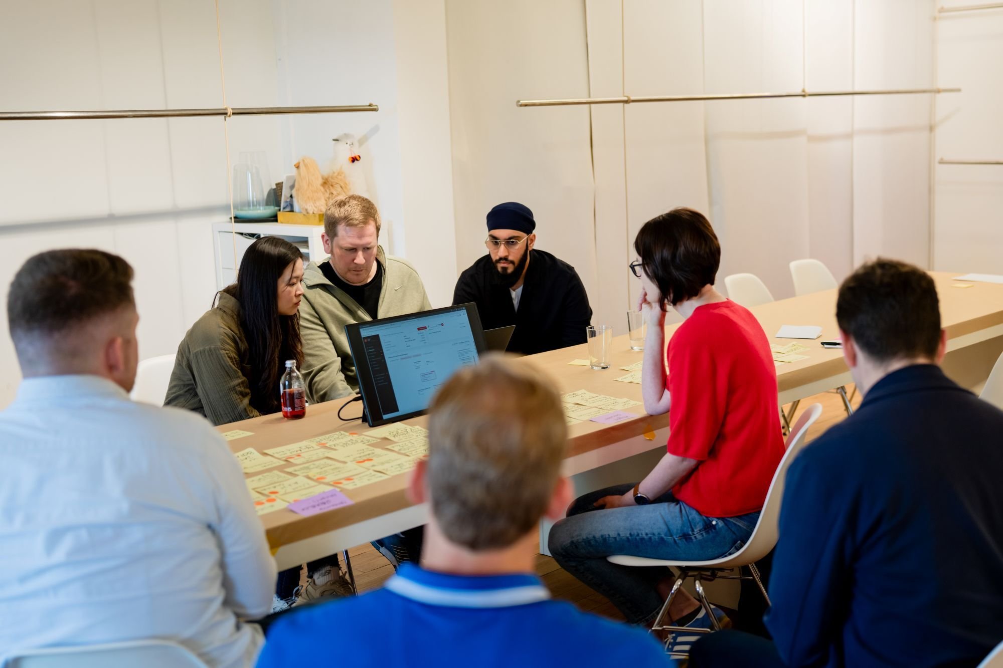 Mehrere Personen sitzen im Workshop um einen Tisch mit Monitor und Haftnotizen.