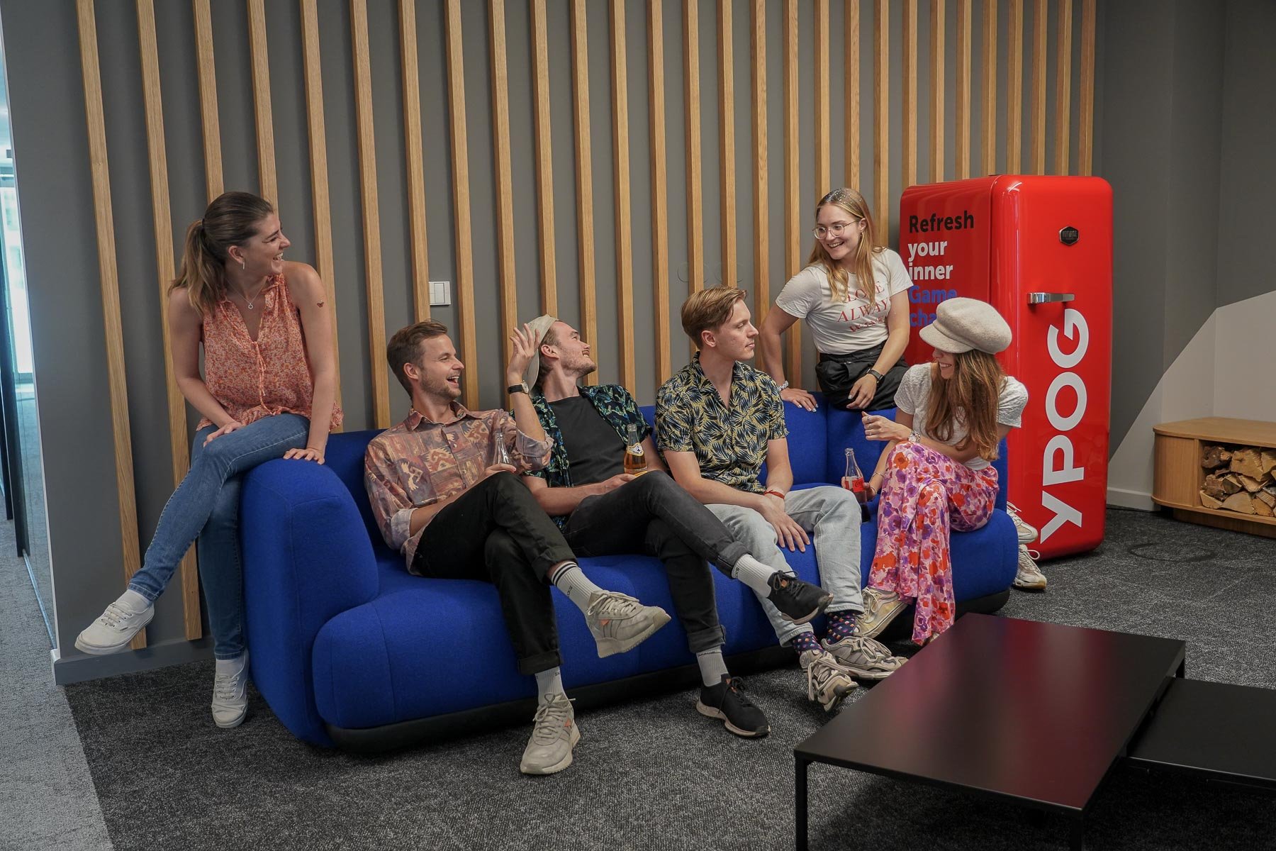 Eine Gruppe von Menschen sitzt auf blauen Sofas in einem Raum.