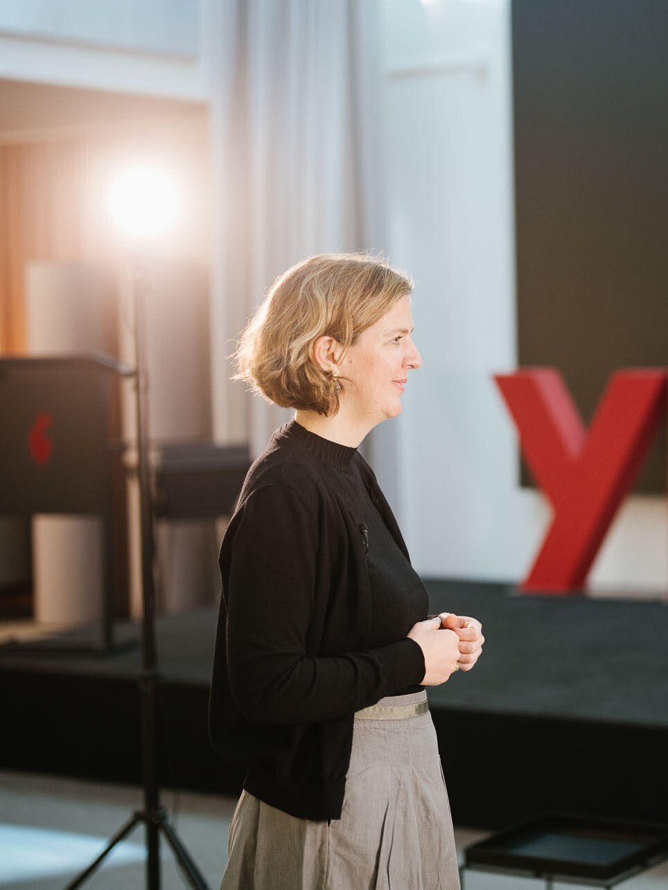 Eine Frau steht und wartet auf ihren Einsatz etwas zu sagen. Im Hintergrund ein Scheinwerfer.